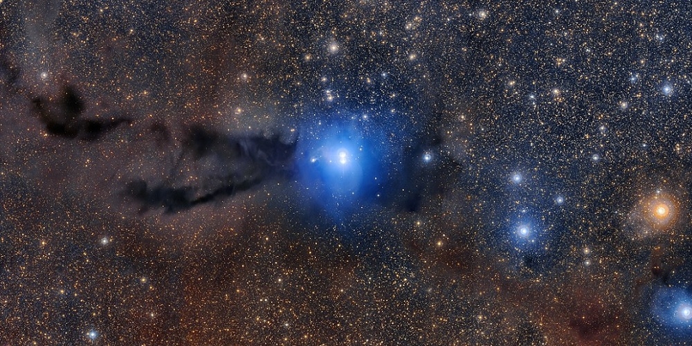 Op deze spectaculaire groothoekopname is een kronkelige donkere wolk van kosmisch stof te zien, die wordt aangelicht door het felle schijnsel van nieuwe sterren.